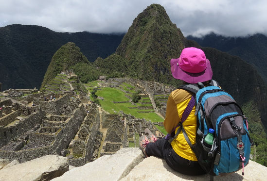 Tourist woman sitting on a rock and looking at Machu Picchu
