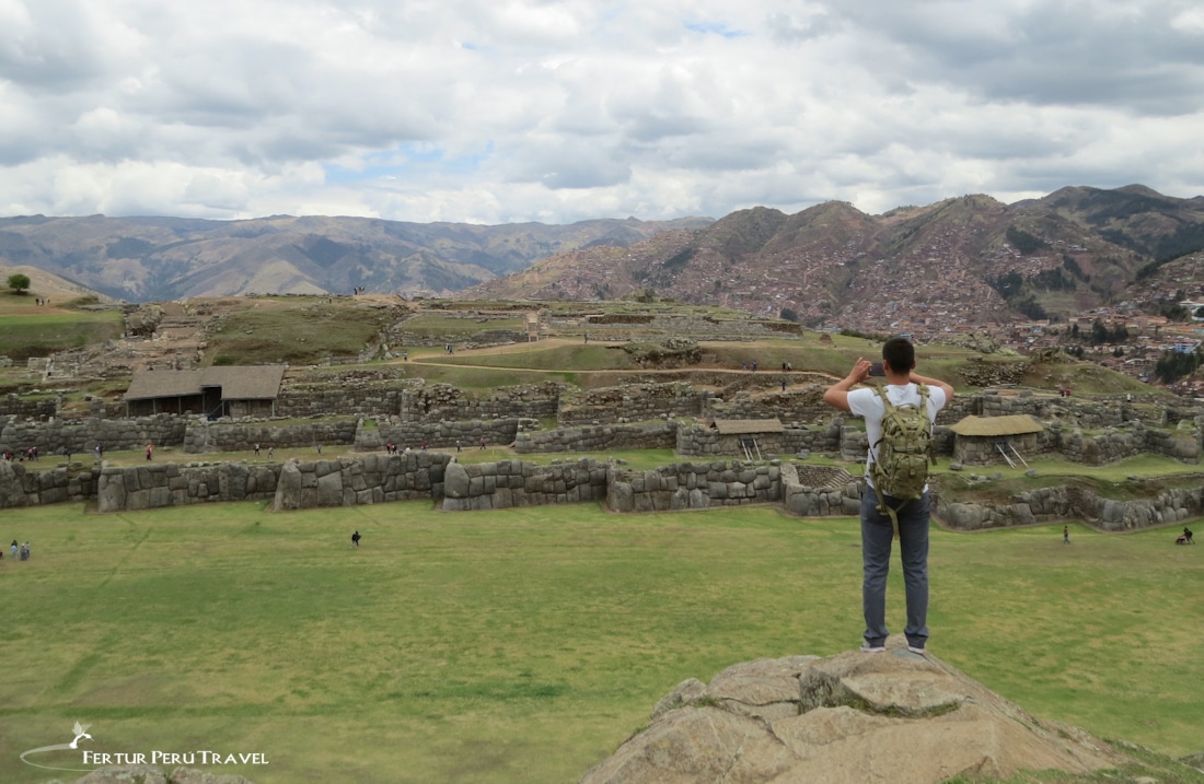 A traveler stands atop a precipice for an overview of the magnificent Inca Temple Fortress of Sacsayhuaman - Cusco Tours by Fertur Peru Travel